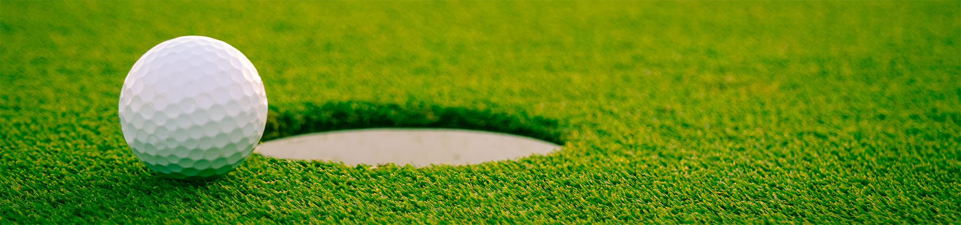 A close-up of a golf ball near the hole on a lush green putting surface, showcasing its detailed texture.