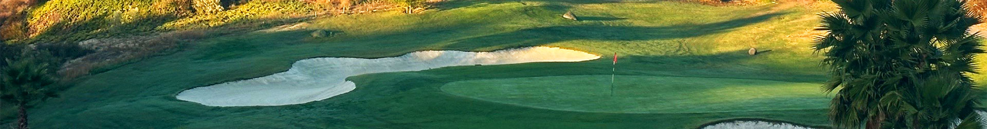 A tranquil golf course landscape featuring lush greenery and a sandy bunker under a clear sky.