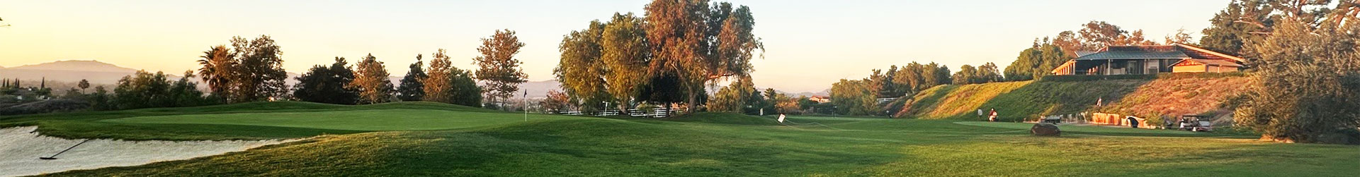 A stunning panoramic view of a golf course bathed in sunset light, showcasing lush fairways and a tranquil pond.